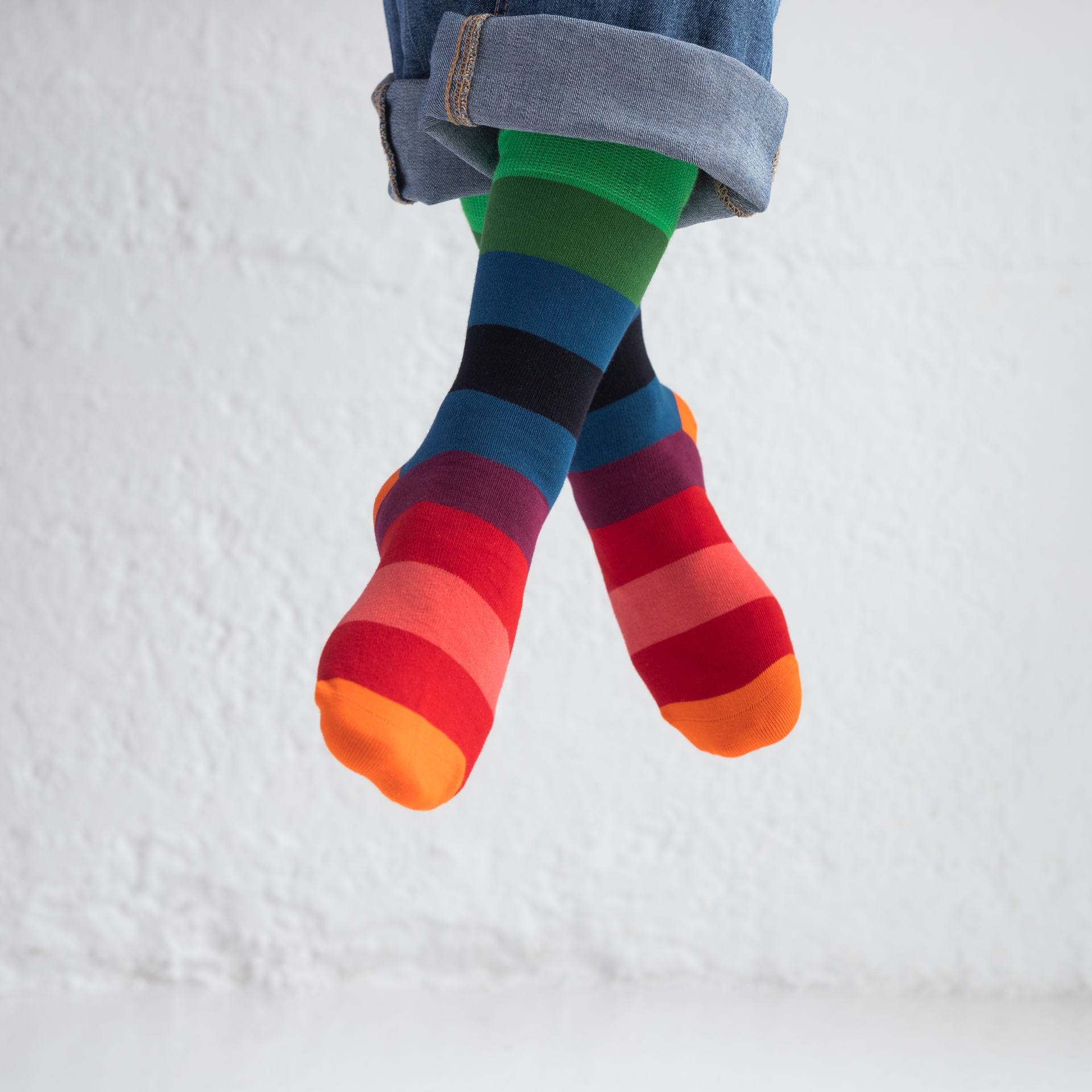 Beine mit hochgekrempelten Jeans und farbenfrohen, gestreiften Socken, Größe 36-41, vor weißem Hintergrund.