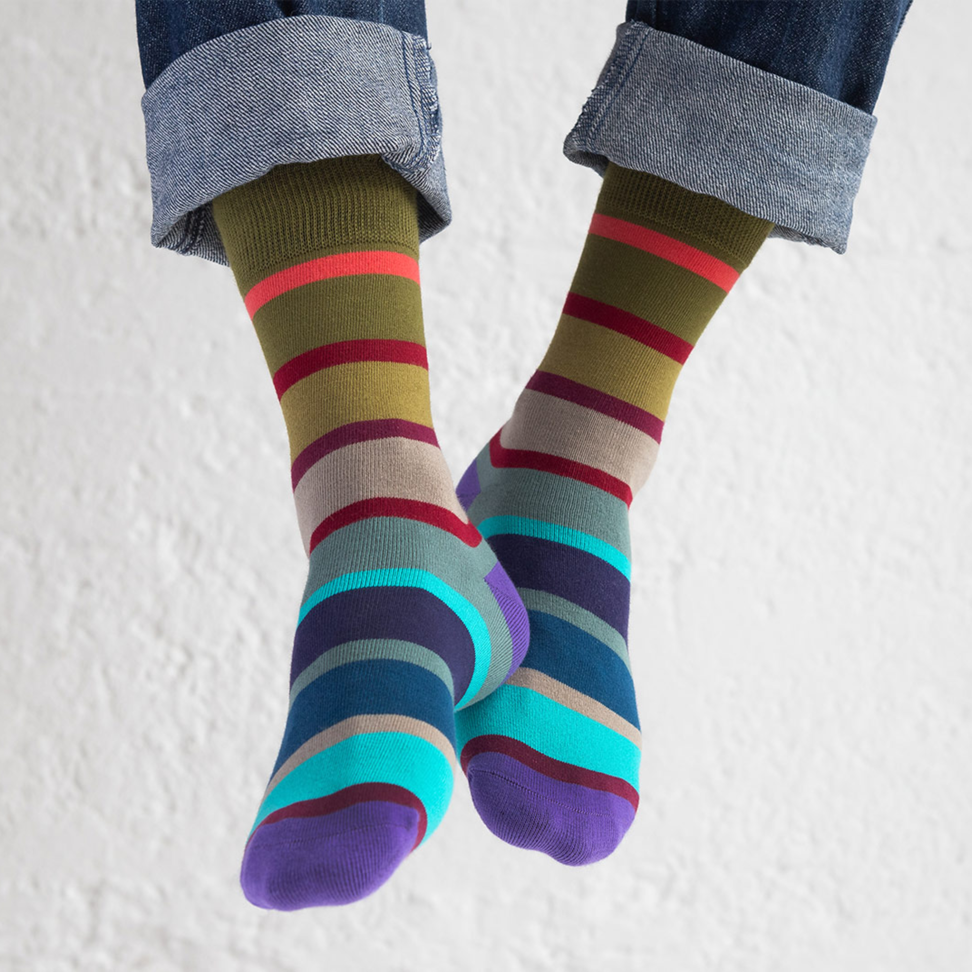 Zwei farbenfrohe Socken mit Ringel-Muster in Olivgrün, Türkis, Blau, Lila, Beige und Rot. Die Socken sind übereinander gelegt.