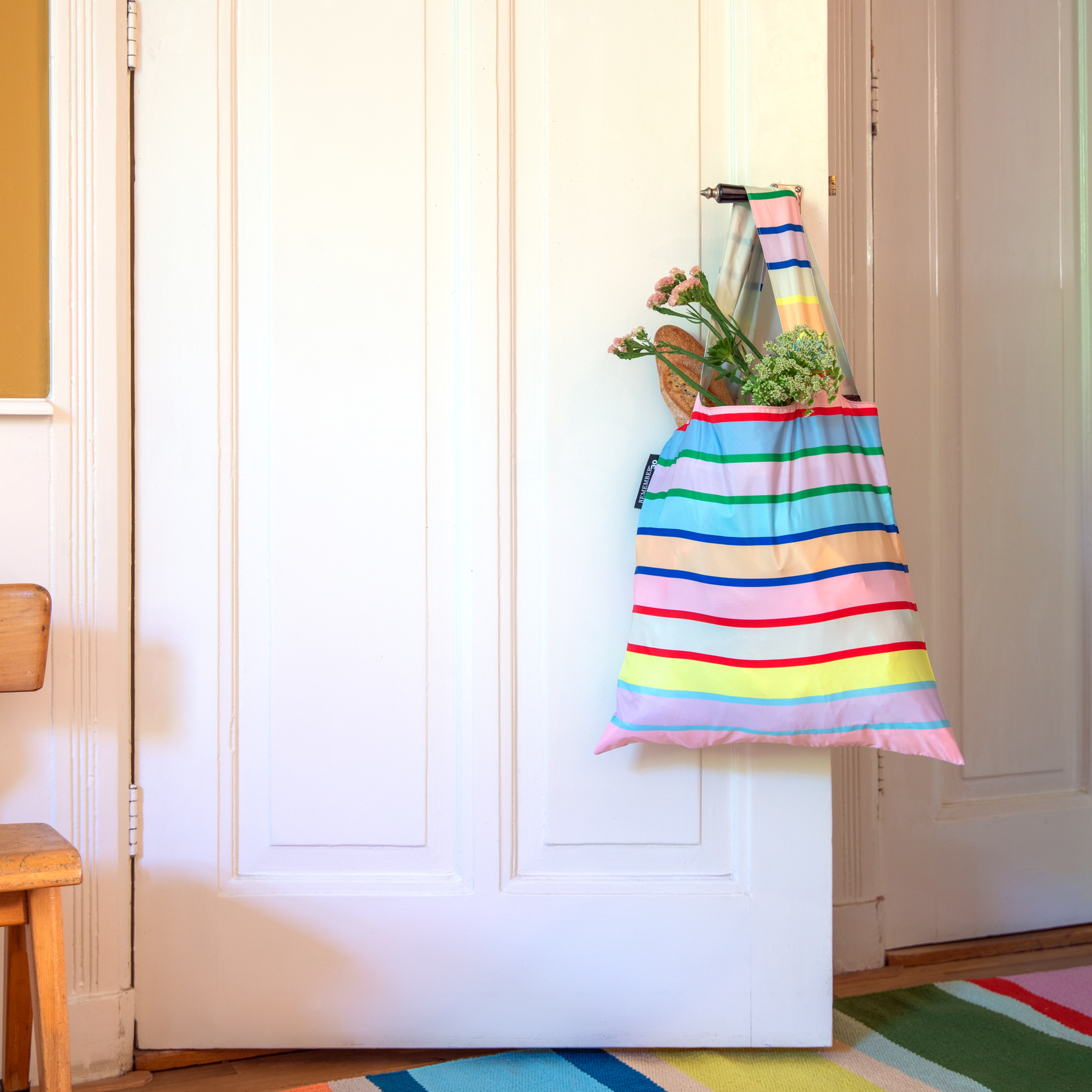 Sac de transport coloré, se tenant debout, orné de rayures horizontales en tons rose, bleu clair, violet, vert, jaune, orange, rouge et bleu foncé. Ans es rayées. Petite étiquette «REMEMBER 30 » cousue sur le côté.