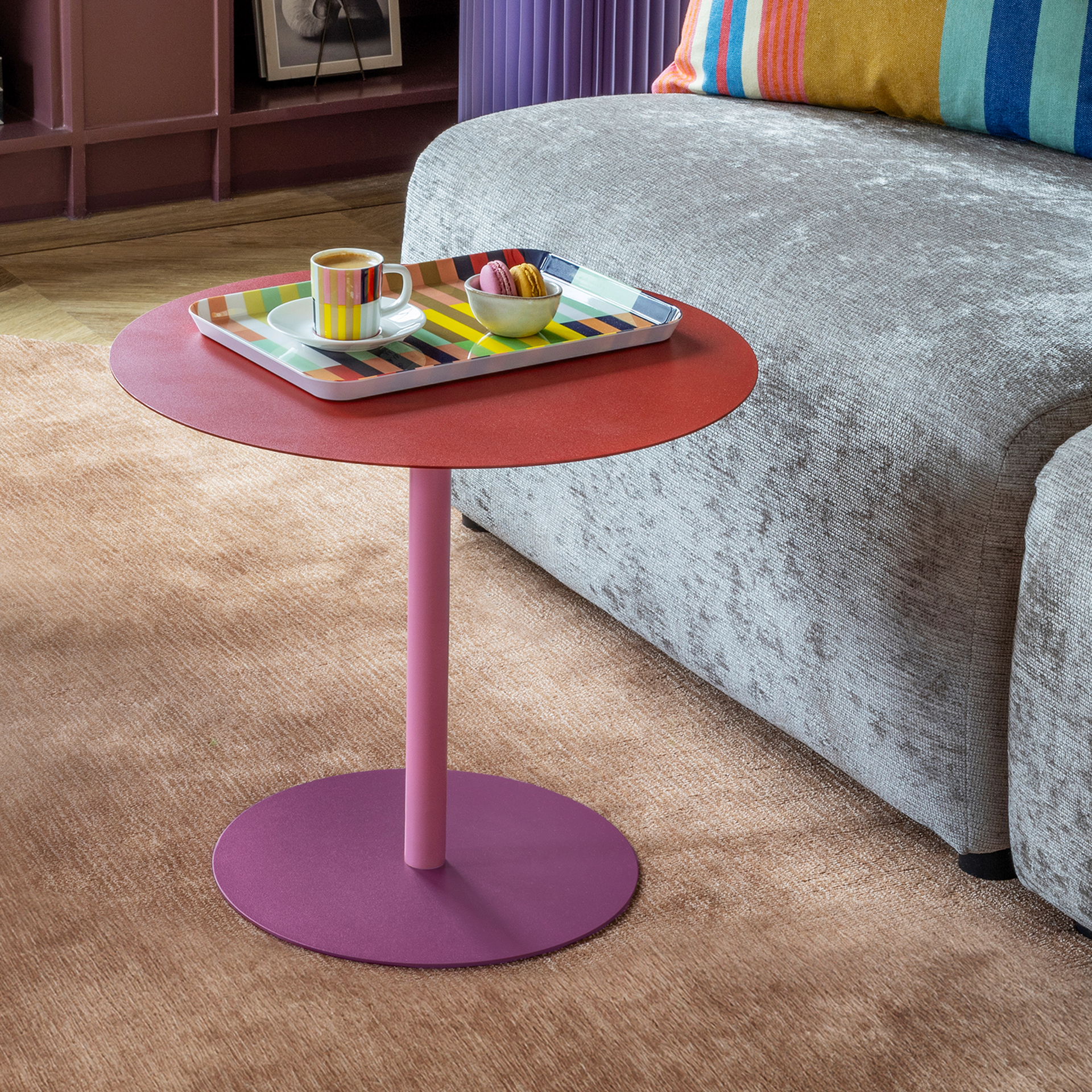 Table d'appoint ronde aux trois nuances de couleur : plateau rouge vif, pied cylindrique rose clair, socle rond violet foncé. Table moderne en métal thermolaqué aux surfaces lisses et mates sur fond blanc.