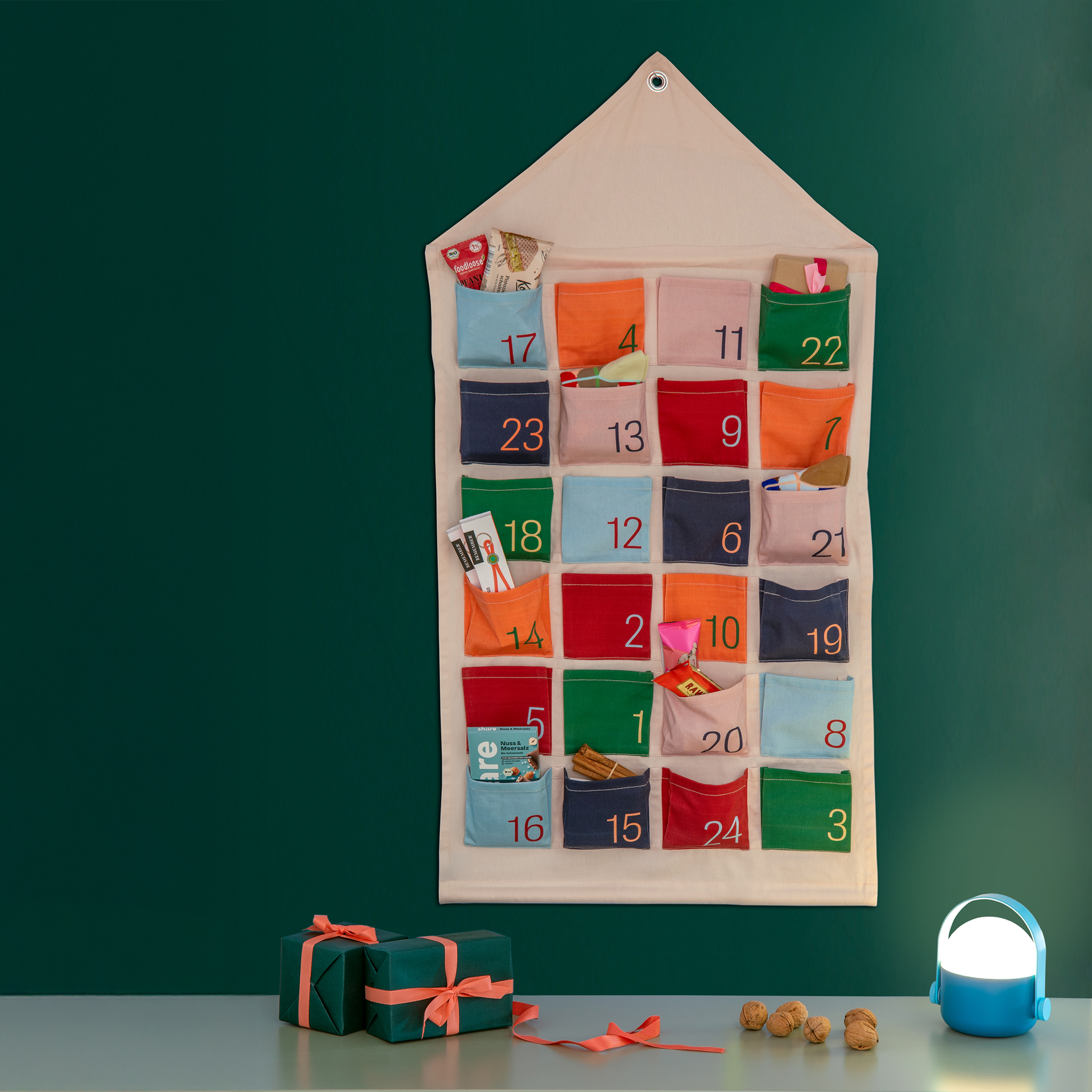 Adventskalender Haus aus Stoff mit 24 bunten Taschen und Zahlen, gefüllt mit kleinen Überraschungen, dekoriert mit Geschenken.
