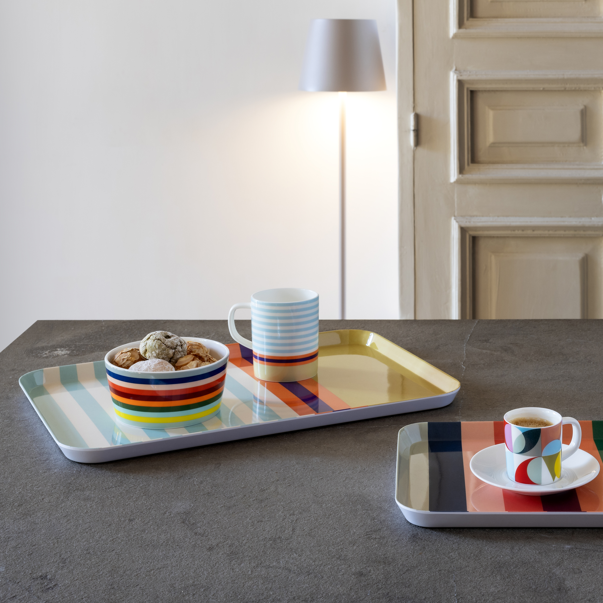 Ein farbenfrohes 'Lorenzo' Müslischalen-Set mit Gebäck auf einem gestreiften Tablett. Im Hintergrund eine passende Tasse und eine Espressotasse mit Untertasse.