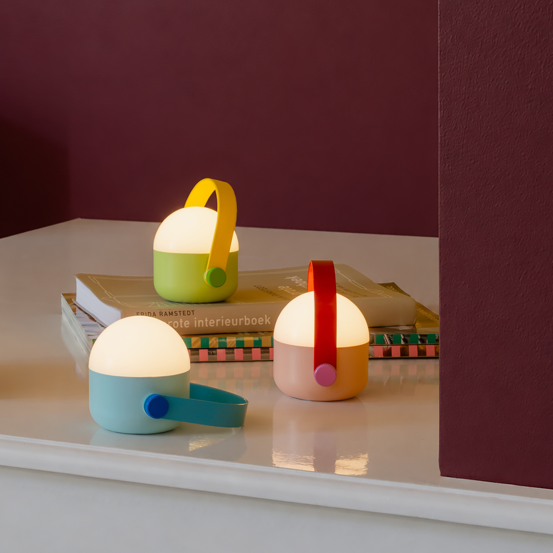 Trois lampes LED colorées à intensité réglable, avec poignées, sont côte à côte. À gauche menthe/poignée turquoise ; au centre vert tilleul/poignée jaune ; à droite rose/poignée rouge. Lumière blanche chaude.