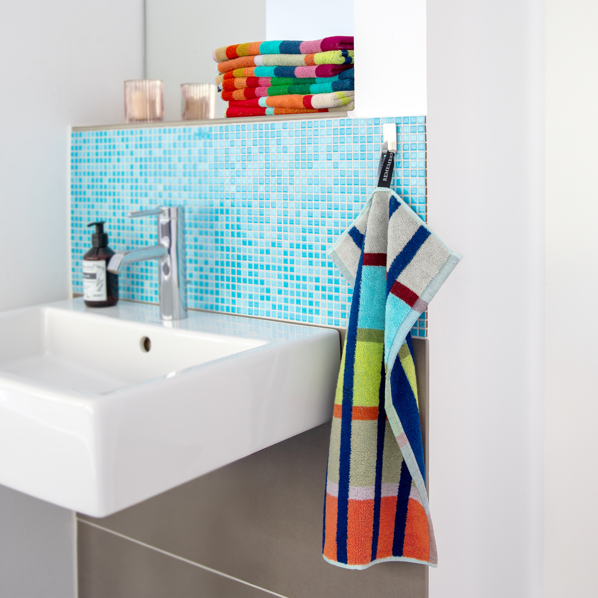 Deux serviettes d'invités Yoku pliées, ornées d'un motif à rayures multicolores très vif. Lignes verticales bleu foncé et larges bandes horizontales blanches, bleu clair, jaunes, vertes, rose saumon et rouge foncé. Coton doux et de qualité.