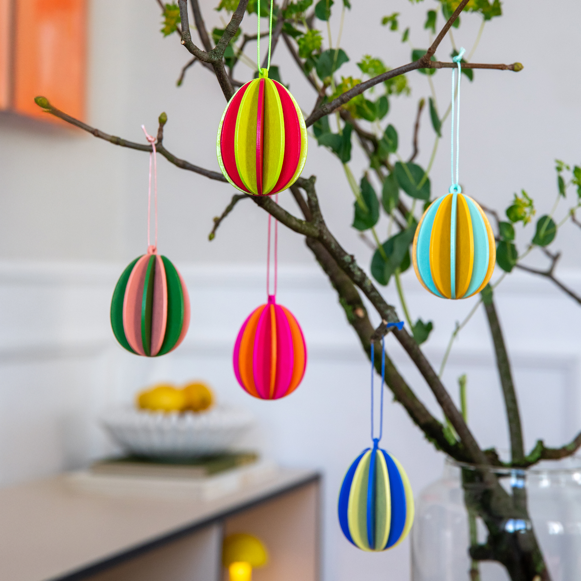 Fünf bunte Baumschmuck-Artikel „Eier“ aus Holz mit Aufhängebändchen. Die Farben sind Gelb, Orange, Blau, Weinrot und Grün.