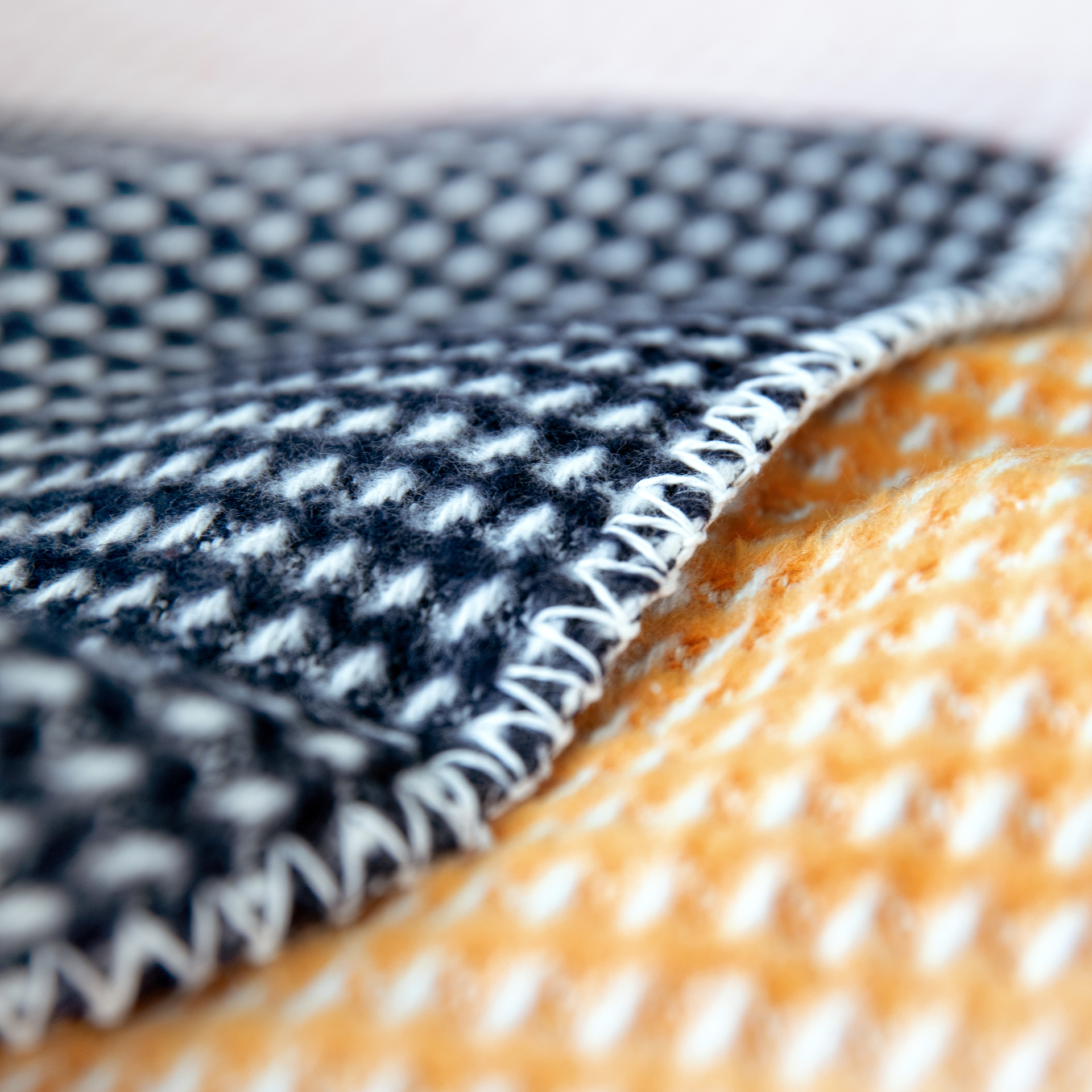 Detailaufnahme der Decke 'Gala': Zwei Stofflagen mit Waffelmuster in Dunkelblau und Orange, verbunden durch einen weißen Zick-Zack-Stich.