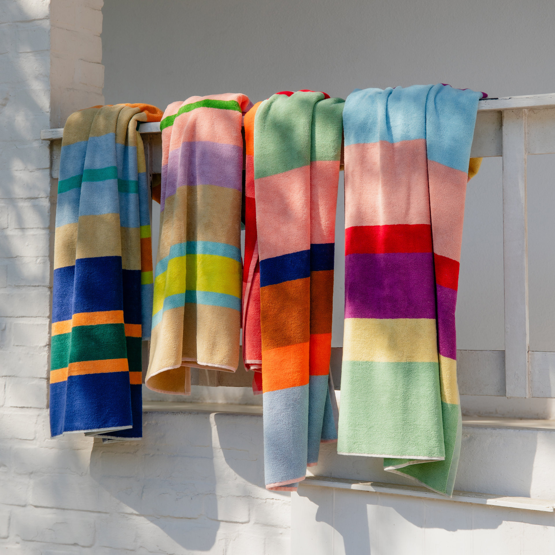 Un drap de bain moelleux 'Tallinn' à rayures multicolores est posé verticalement sur un fond blanc. Les couleurs des rayures sont le jaune, l'orange, le vert, le rouge, le bleu et le beige.