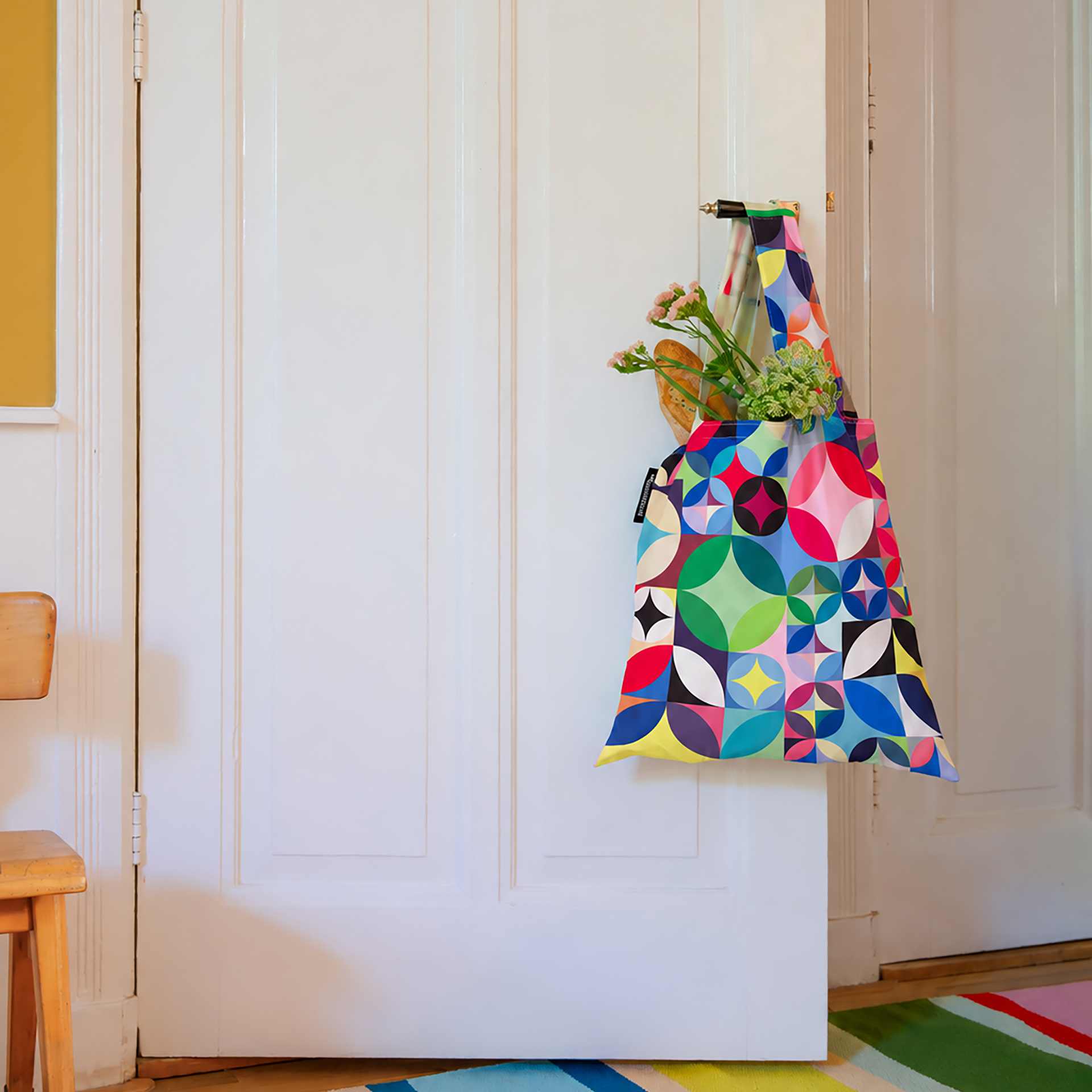 Sac de transport pliable aux couleurs vives, orné d’un motif géométrique « Rosetta » de cercles et quarts de cercle en tons rouge, bleu, vert, jaune, rose, noir et blanc. Deux poignées sur fond blanc et banderole bleue « 30 ».