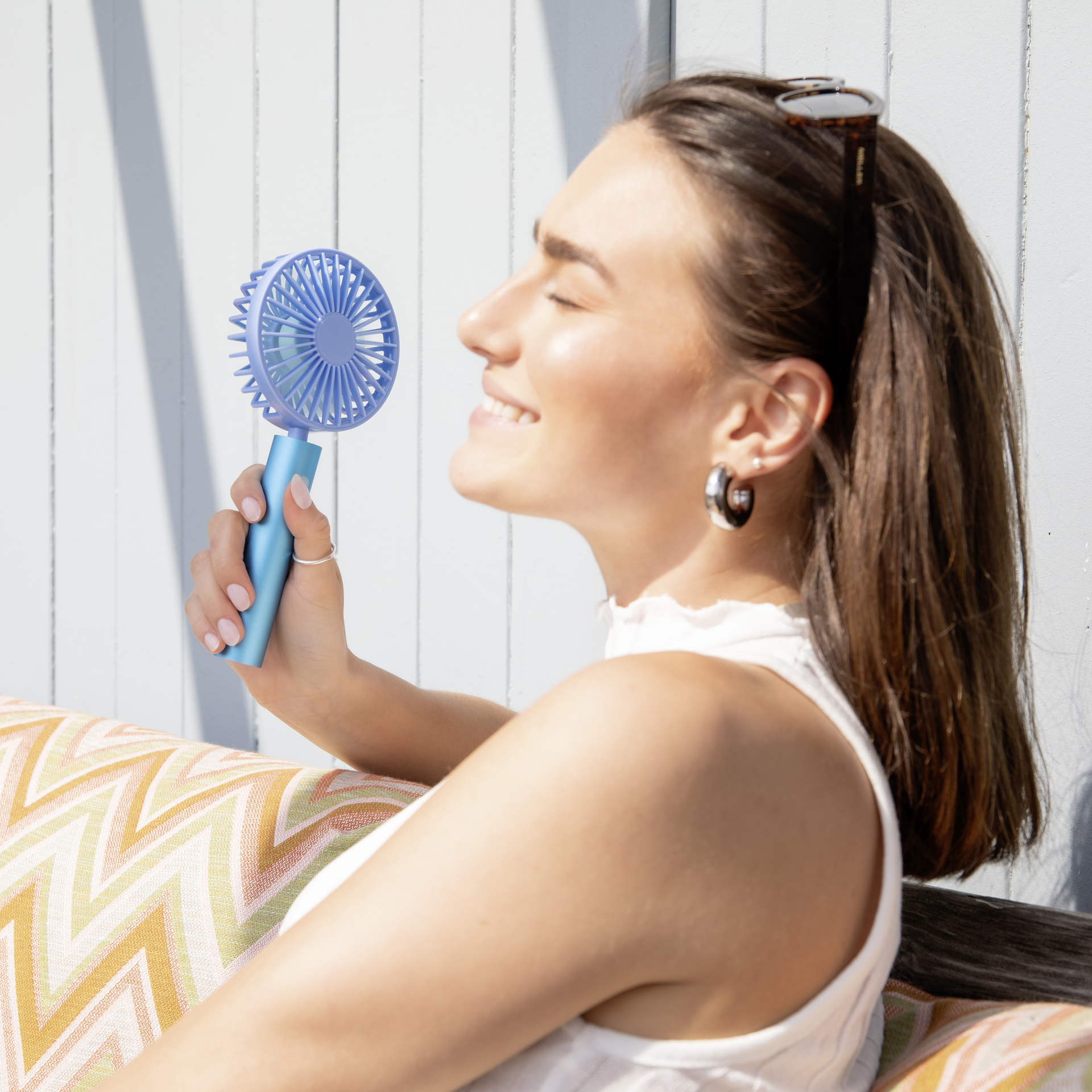 Un ventilateur portable de couleur aqua avec une tête pivotante et une grille ronde qui protège les pales du rotor. La poignée est cylindrique avec un bouton.