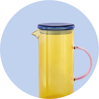 Eine leuchtend gelbe Glaskaraffe mit einem dunkelblauen Deckel und einem rosafarbenen Griff, die vor einem hellblauen Hintergrund steht. Die Karaffe ist transparent und hat eine schlanke, zylindrische Form.