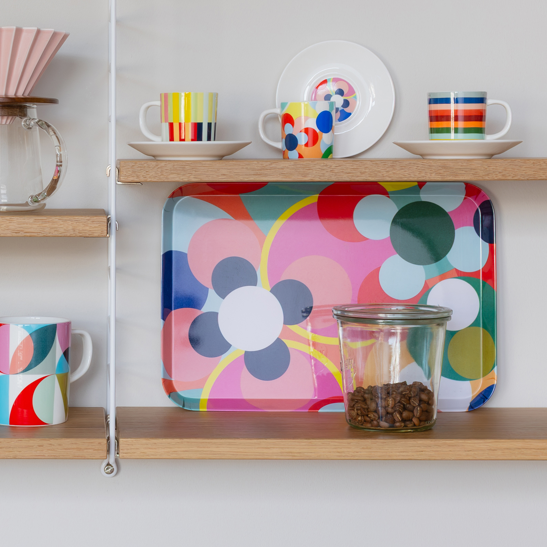 Ein Regal mit Kaffeetassen, Tellern, einer Kaffeekaraffe, einem bunten Tablett und einem Glas mit Kaffeebohnen.