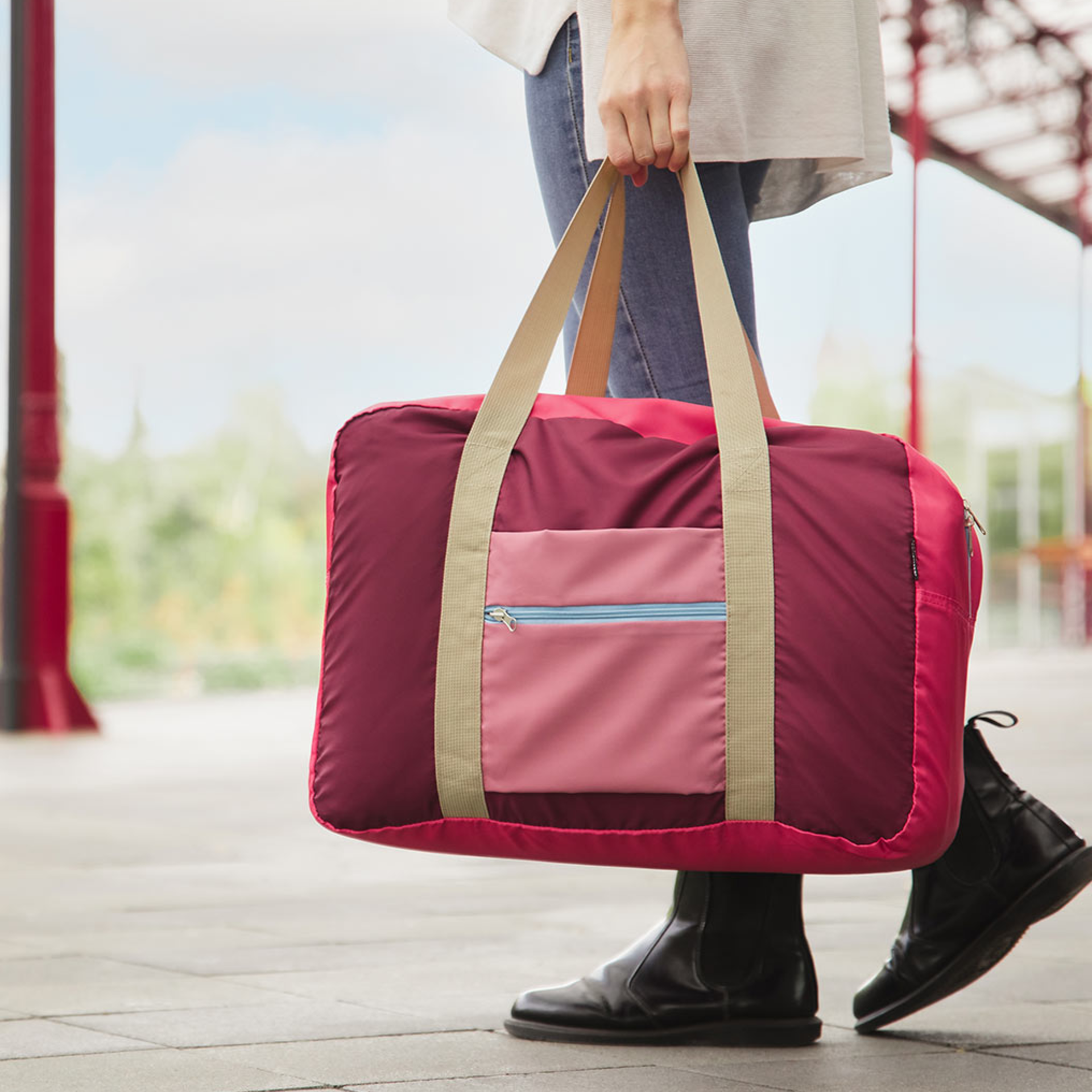 Rechteckige Reisetasche 'Ida' in Rot- und Pinktönen, mit Tragegriffen aus beigem Gurtband und einem Reißverschlussfach auf der Vorderseite.