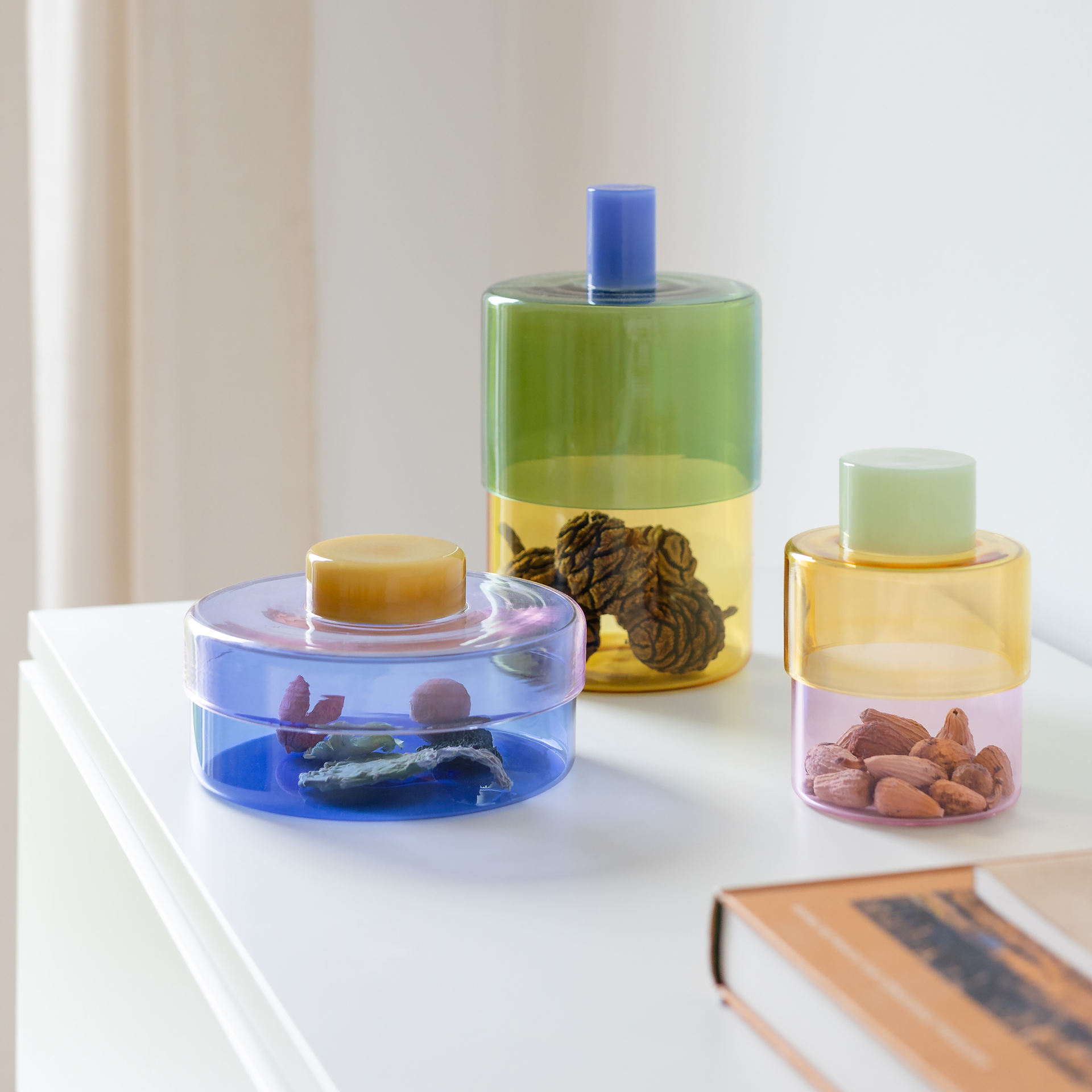 Boîte en verre cylindrique Milou avec couvercle opaque vert clair. Corps transparent en deux parties : haut jaune vif, bas rose tendre. Verre borosilicaté apte au contact alimentaire, rangement élégant.