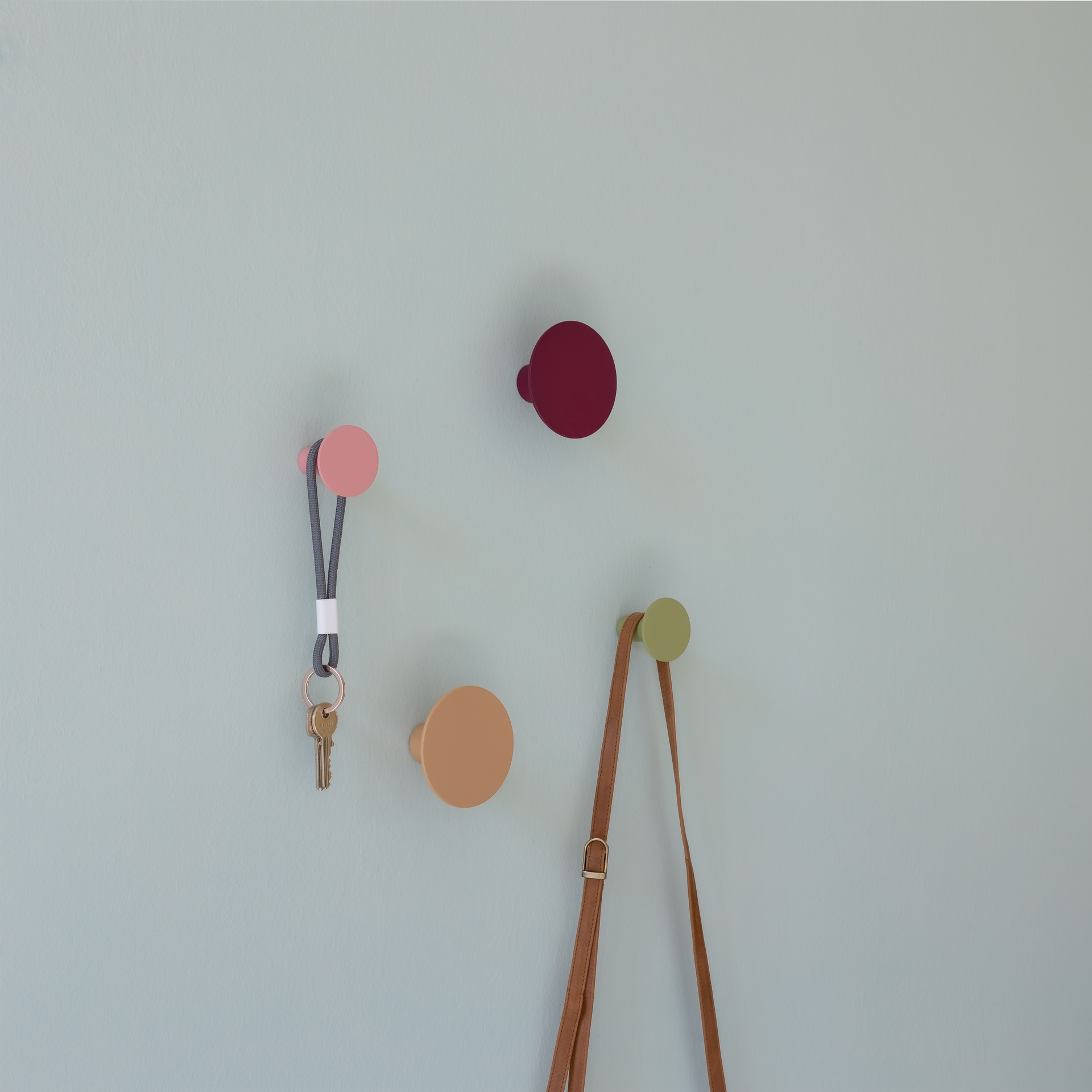 Mehrfarbiges Wandhaken-Set: Zwei große Haken in Beige und Bordeaux, zwei kleine Haken in Rosa und Mintgrün auf weißem Grund.