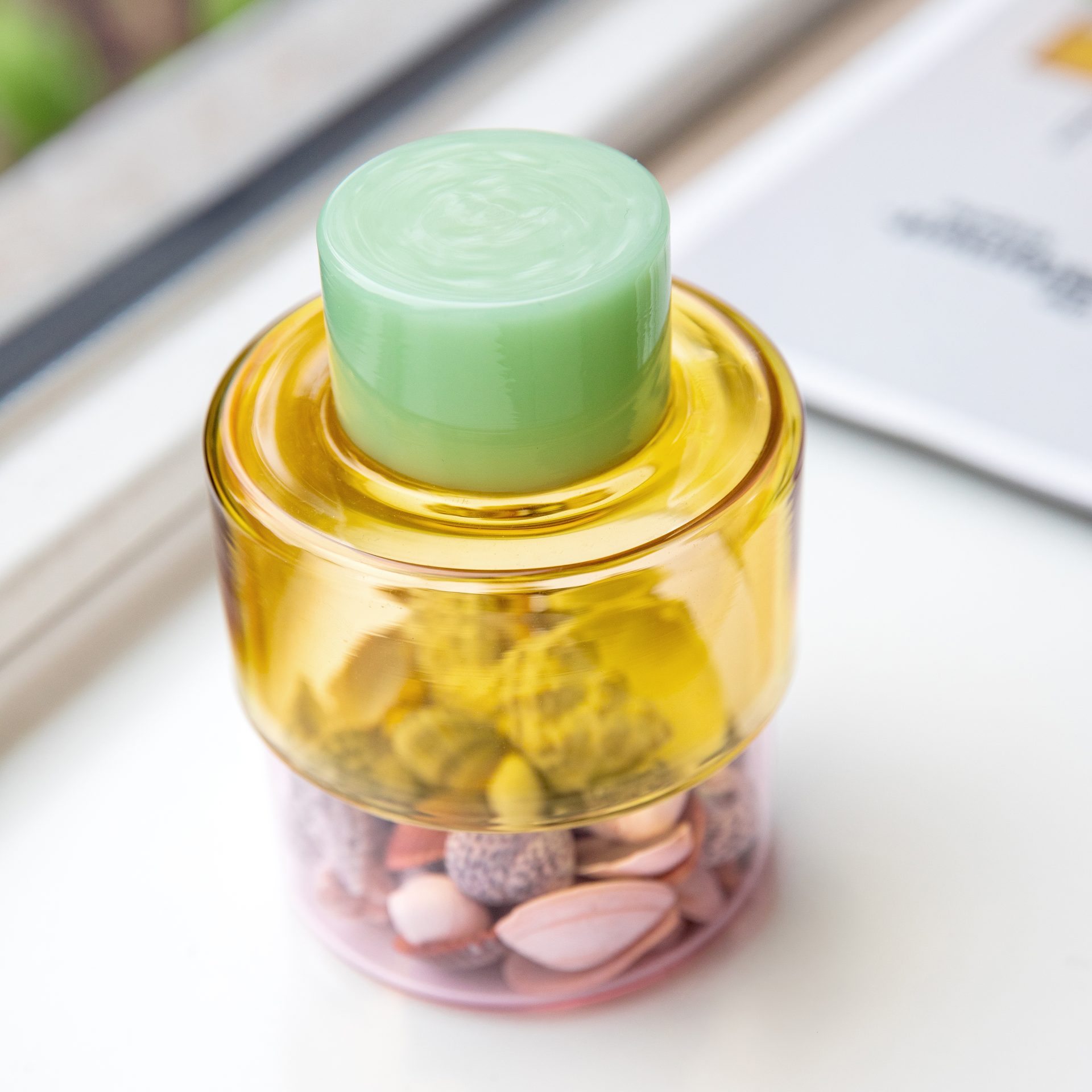 Barattolo cilindrico Milou con coperchio opaco verde chiaro. Corpo trasparente diviso in due: parte superiore giallo brillante e inferiore rosa delicato. In vetro borosilicato, idoneo al contatto alimentare, elegante contenitore.