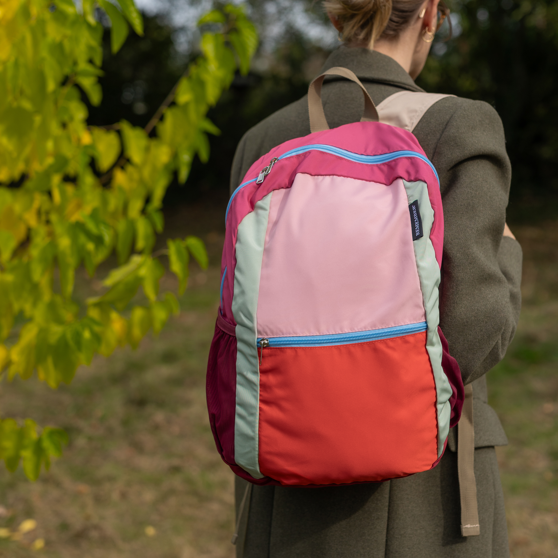 Zaino pieghevole colorato nei toni del rosa, fucsia, verde menta e arancione, realizzato in poliestere leggero. Dotato di tasca frontale con cerniera azzurra, tasche laterali in rete color bordeaux e spallacci beige. Etichetta " REMEMBER" sul davanti.