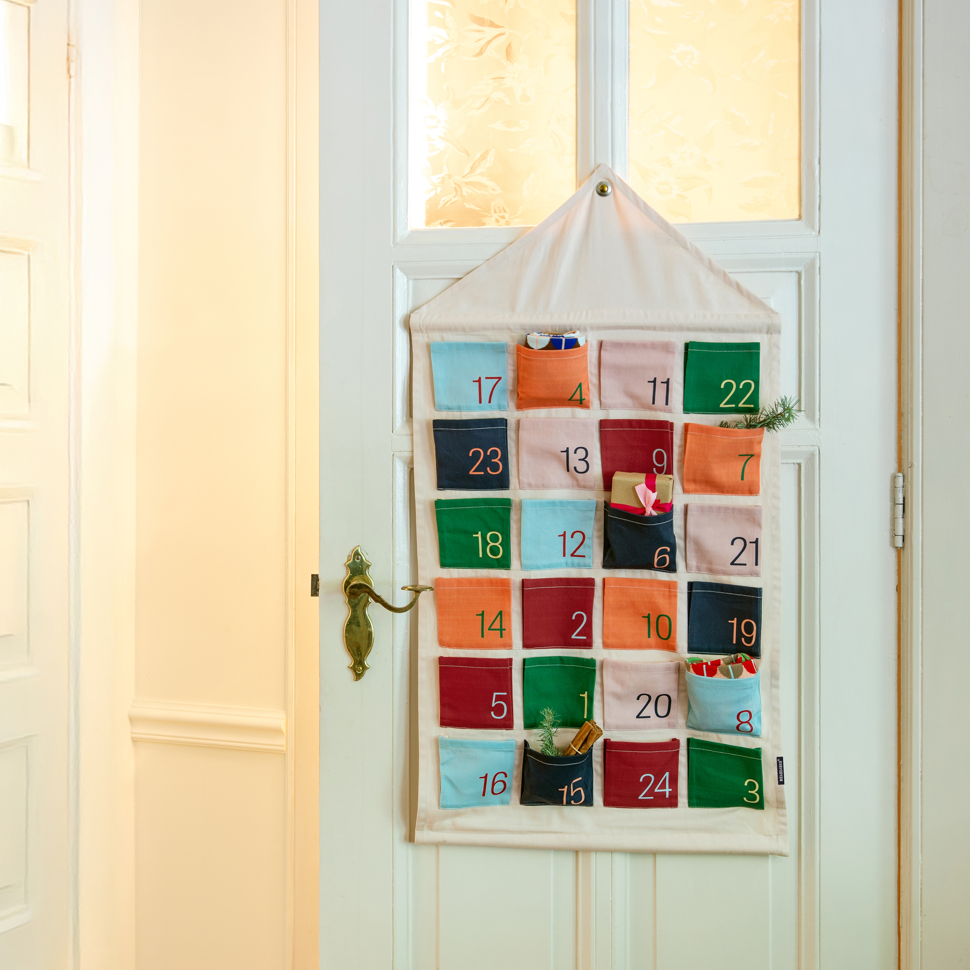 Textil-Adventskalender im Hausdesign mit 24 farbigen Taschen. Jede Tasche ist mit einer Zahl versehen. Das Haus ist beige.