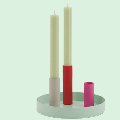 Zwei beigefarbene Kerzen in farbigen Haltern (beige, rot, pink) auf einem runden, mintgrünen Tablett vor mintfarbenem Hintergrund.