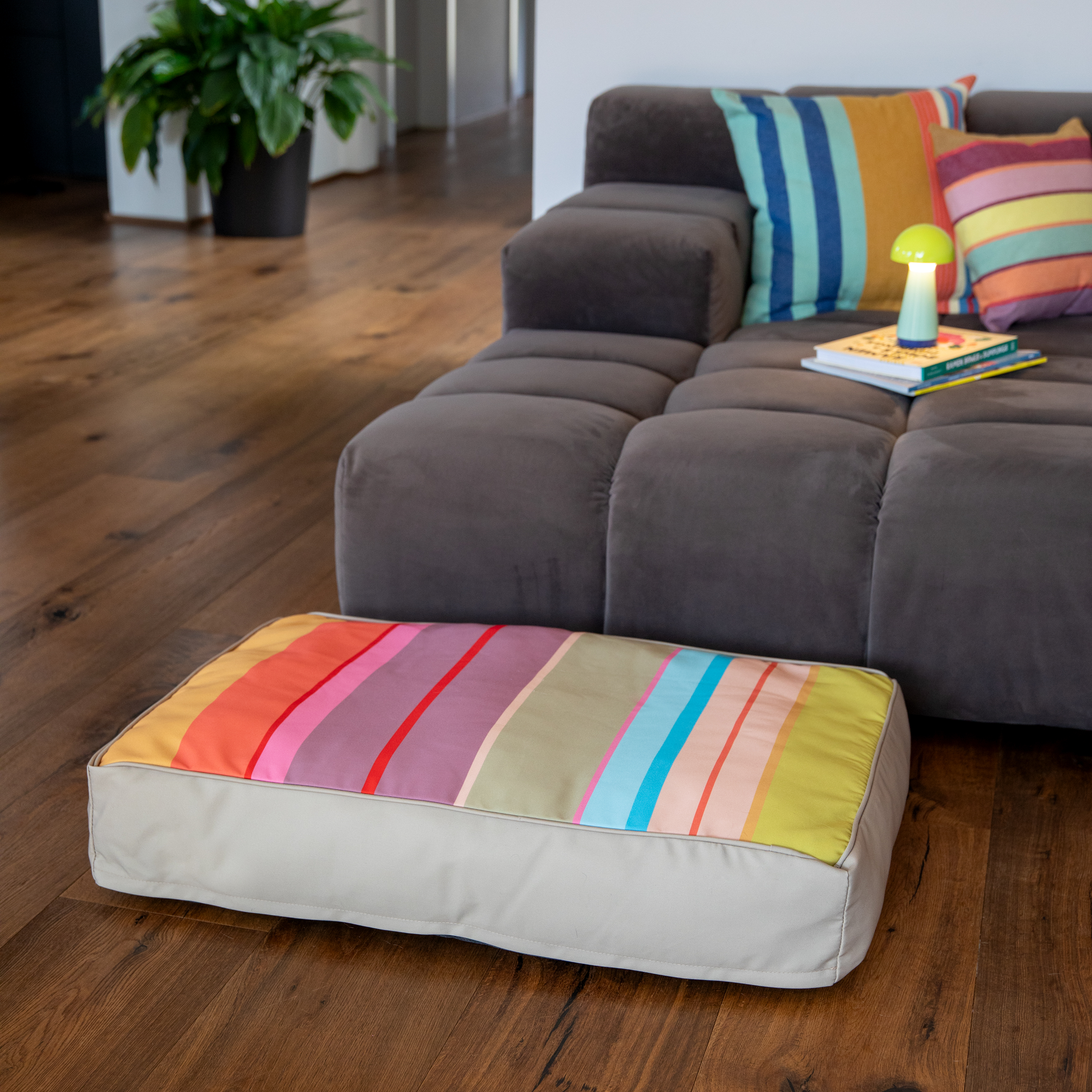 Coussin rectangulaire pour chien Theo M avec une face supérieure colorée : larges rayures horizontales dans des tons vifs de jaune, orange, rouge, rose, violet, vert et bleu clair. Côtés dans un beige clair neutre. Idéal comme lieu de repos.
